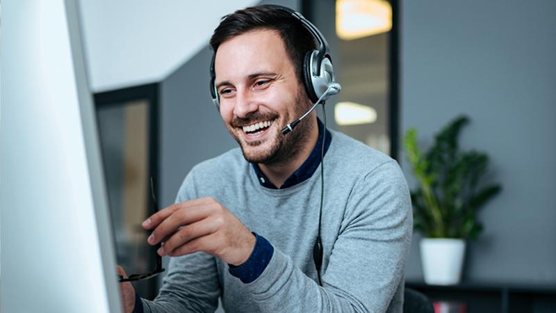 A customer service agent speaks on a headset while sitting in front of a monitor.