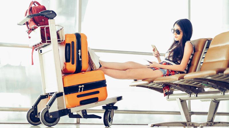 Generation Z traveler looking at phone while waiting at the airport with luggage